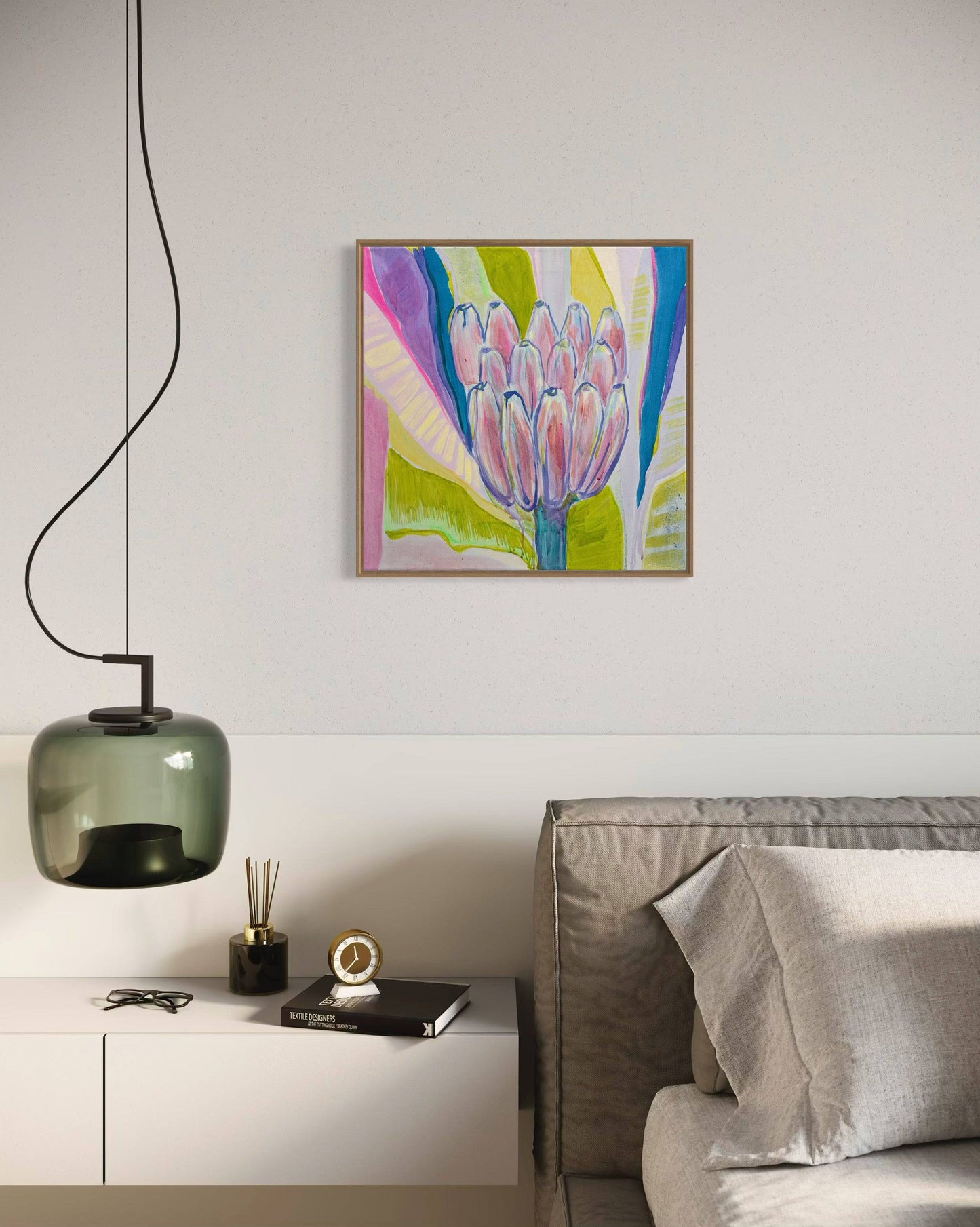 Modern bedroom corner with neutral bedding, white nightstand, green glass pendant light, and colorful botanical painting by Kathryn Sillince
