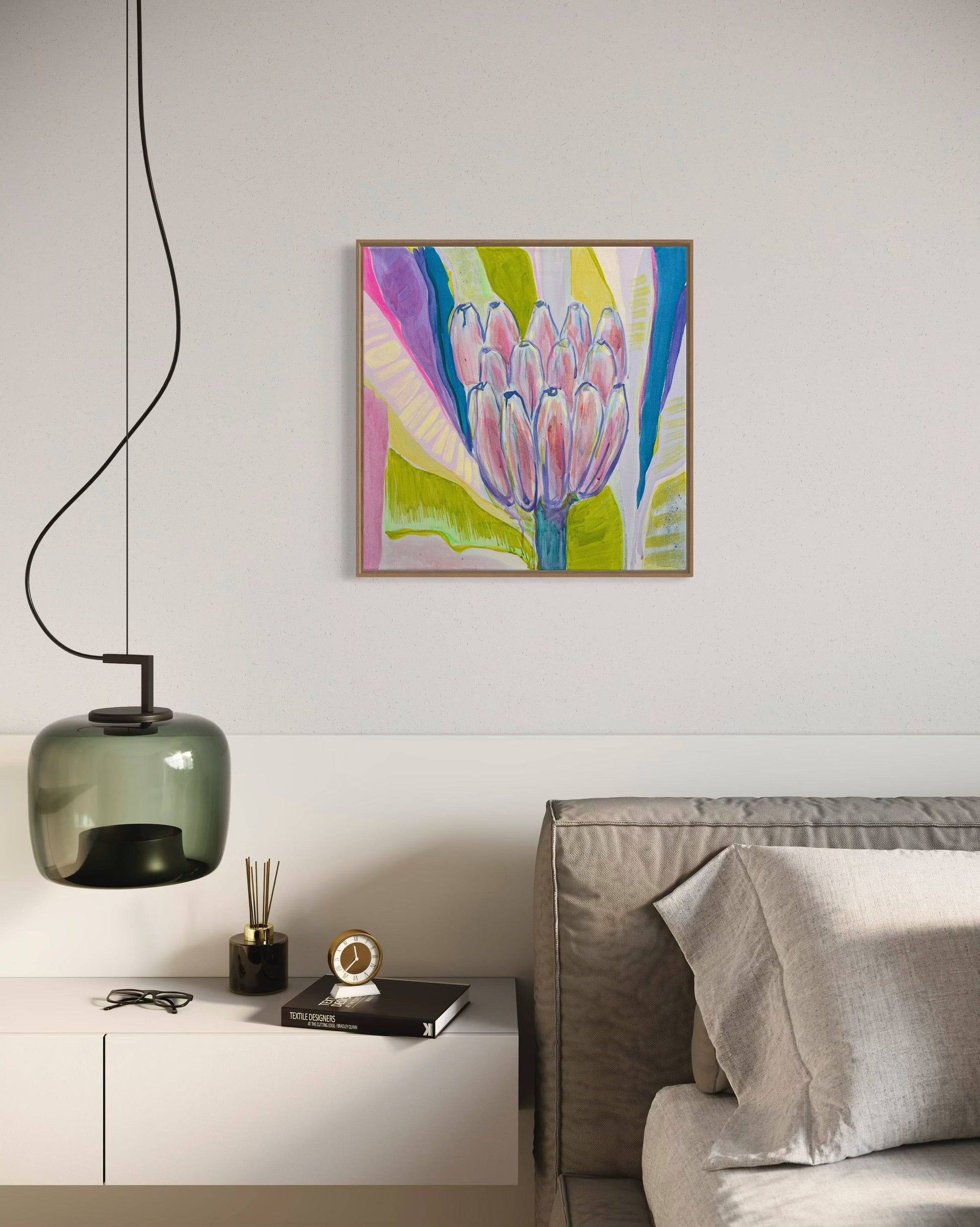Modern bedroom corner with neutral bedding, white nightstand, green glass pendant light, and colorful botanical painting by Kathryn Sillince