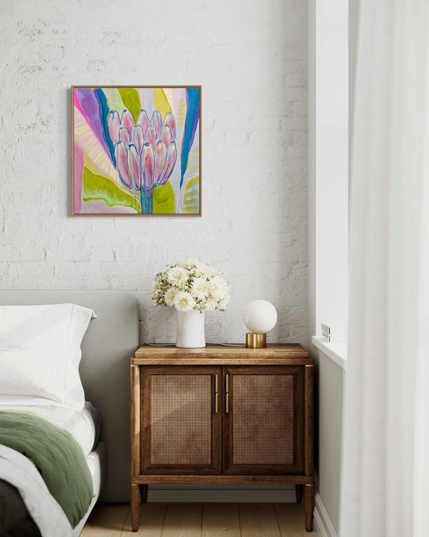 Modern bedroom corner with botanical abstract painting by Kathryn Sillince above wooden nightstand with vase of white flowers and lamp