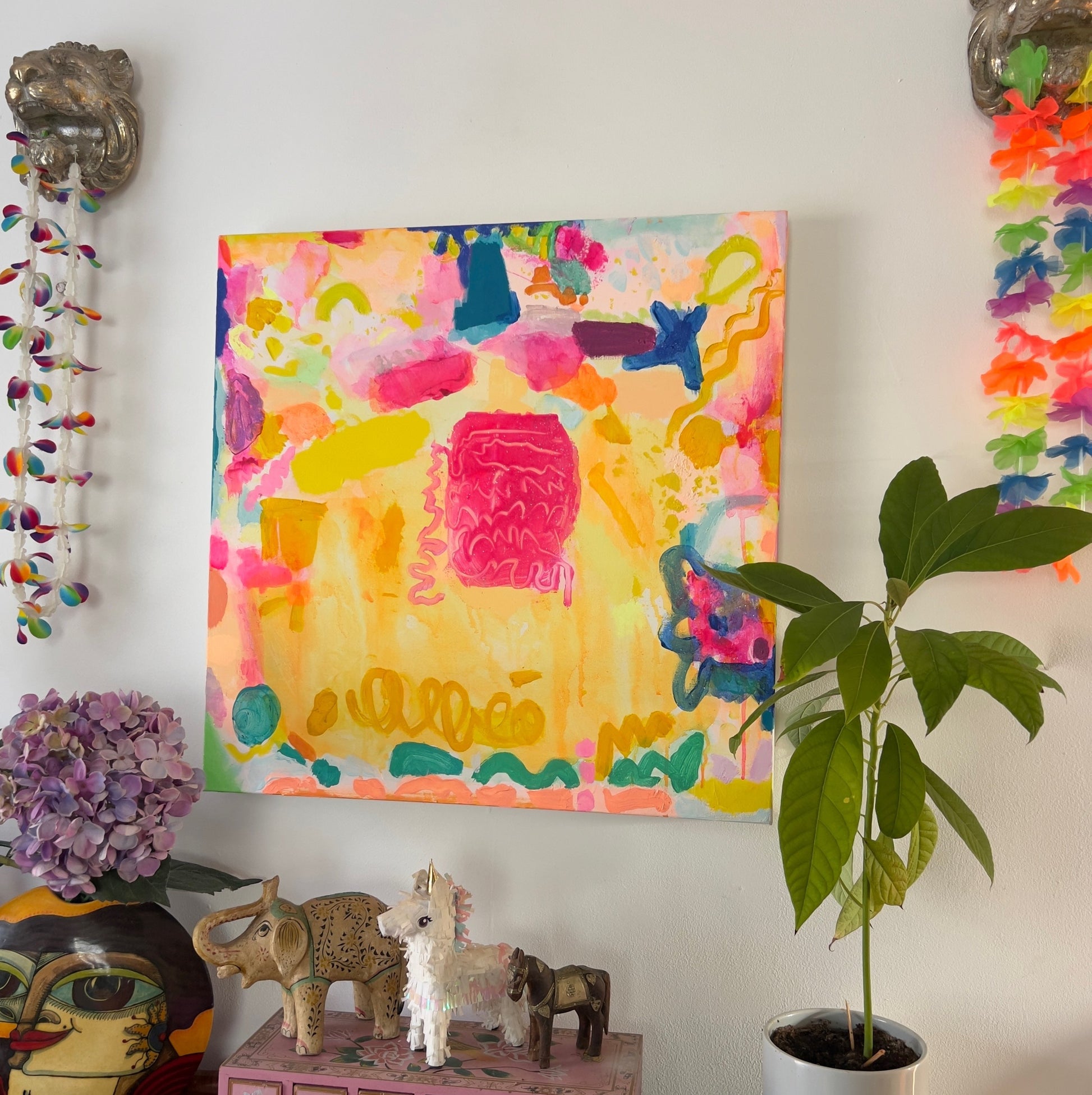 Colorful abstract painting on a wall with decorative items and a plant below.